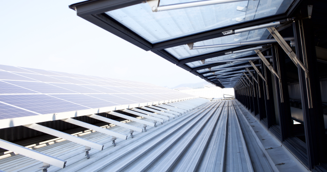 Close-up view of solar panels installed on a modern industrial metal rooftop with open skylight structures.
